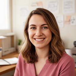 Sarah Mills smiling in a small office with a notebook and a wall of task sketches