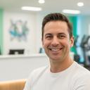 A gym owner smiling beside a reception desk in a bright fitness studio