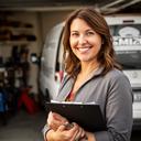 Smiling woman in a workshop holding a clipboard beside a service van